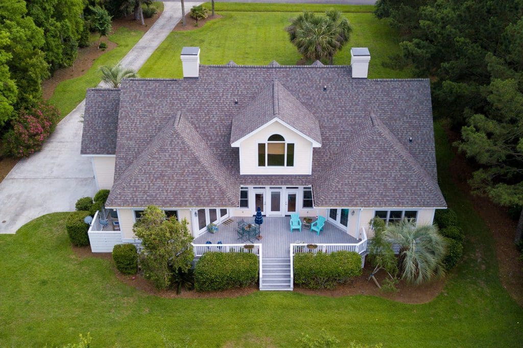 Aerial view of large home with new roof on wooded grassy property
