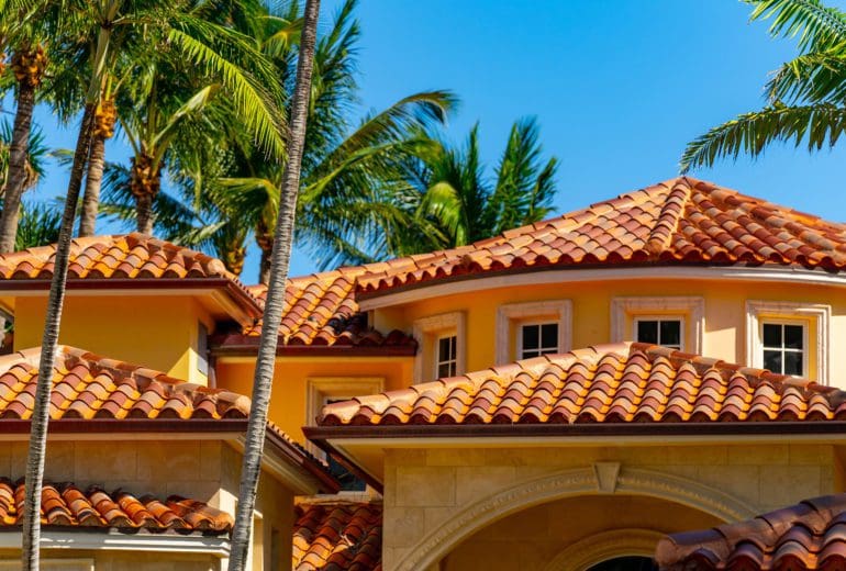 Barrel tile roof top luxury Florida home with colorful palms and blue sky