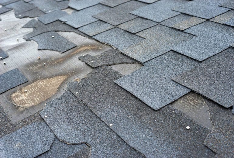 Сlose up view of bitumen shingles roof damage that needs repair.