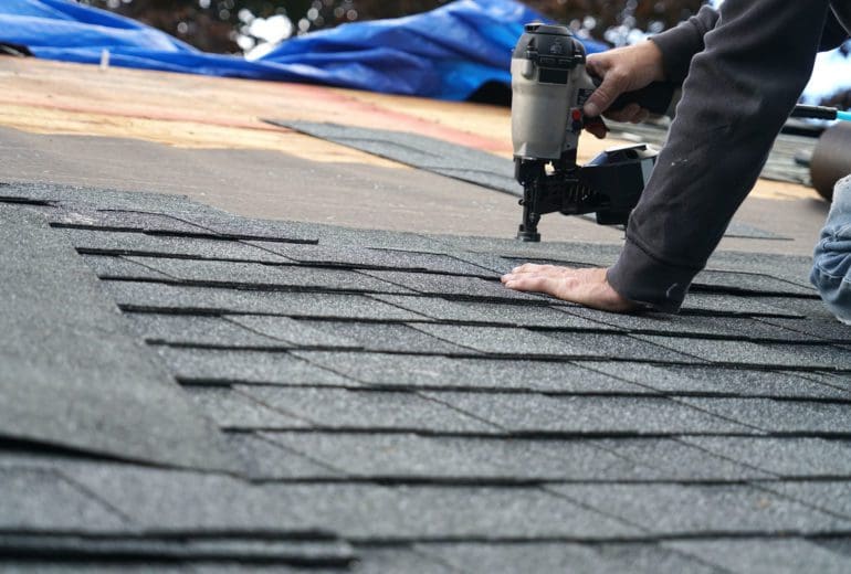 handyman using nail gun to install shingle to repair roof