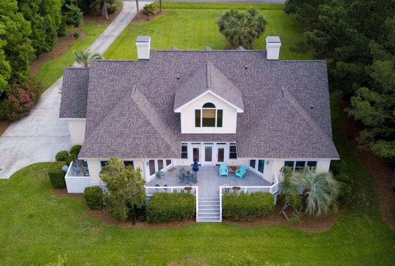 Aerial view of large home with new roof on wooded grassy property