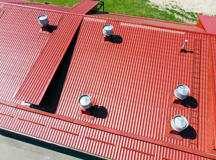 new red metal commercial warehouse roof with installed pipes of ventilation systems