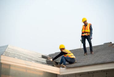 Roofer worker in protective uniform wear and gloves, installing concrete roof tile on top of the new roof of residential building under construction.