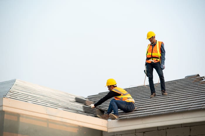 Roofer worker in protective uniform wear and gloves, installing concrete roof tile on top of the new roof of residential building under construction.