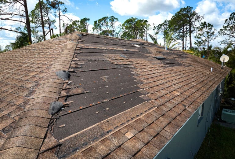 Damaged house roof with missing shingles after hurricane Ian in Florida.