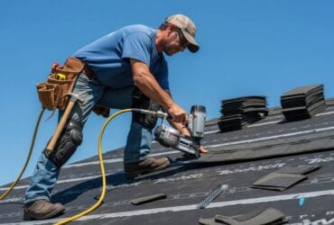 Roofer installing new shingles on a residential house roof with a nail gun construction