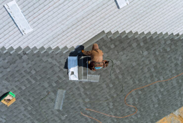 Worker uses an air hammer to nail new shingles bitumen for roof