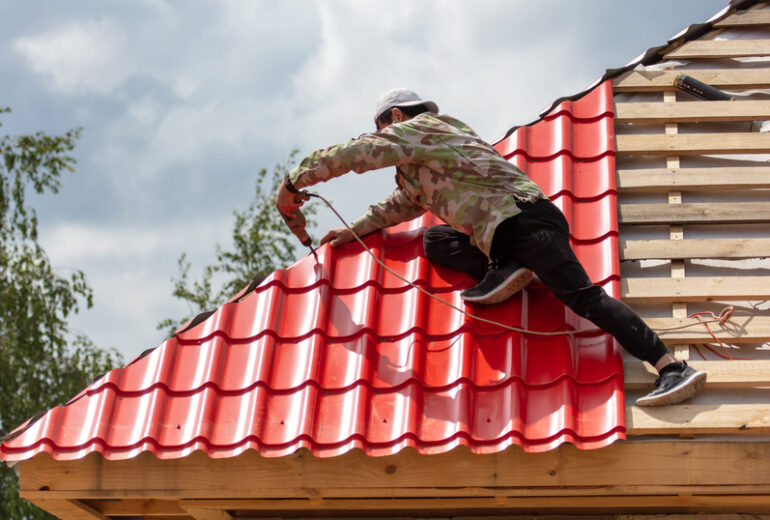 Workers install red metal tiles on the roof of the house.